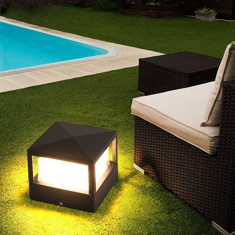 Firkantet sort lampe med pyramideformet låg lyser på en græsplæne ved en pool og en rottingsofa. 4
