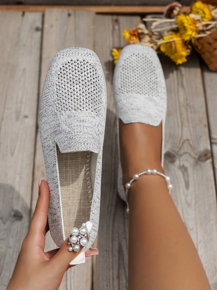 Lysegrå mesh slip-on sko set oppefra, hvor en hånd holder den ene sko og viser indersålen. 15