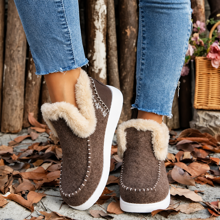 Brune slip-on sneakers med plysskaft og broderet snefnug på hælen, set bagfra og fra siden på model. 2
