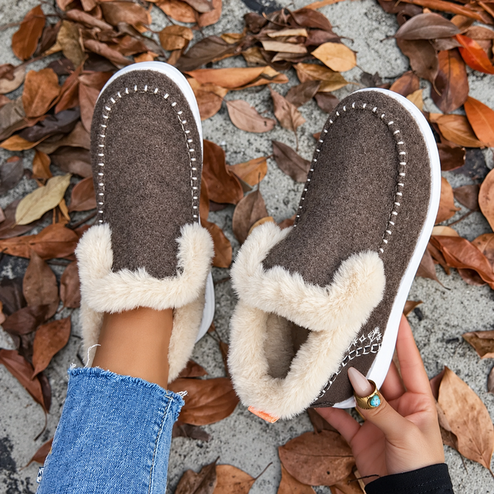Brune sneakers set oppefra med hvide kantsting og plysindvendig, den ene holdt i hånden og den anden på foden. 8