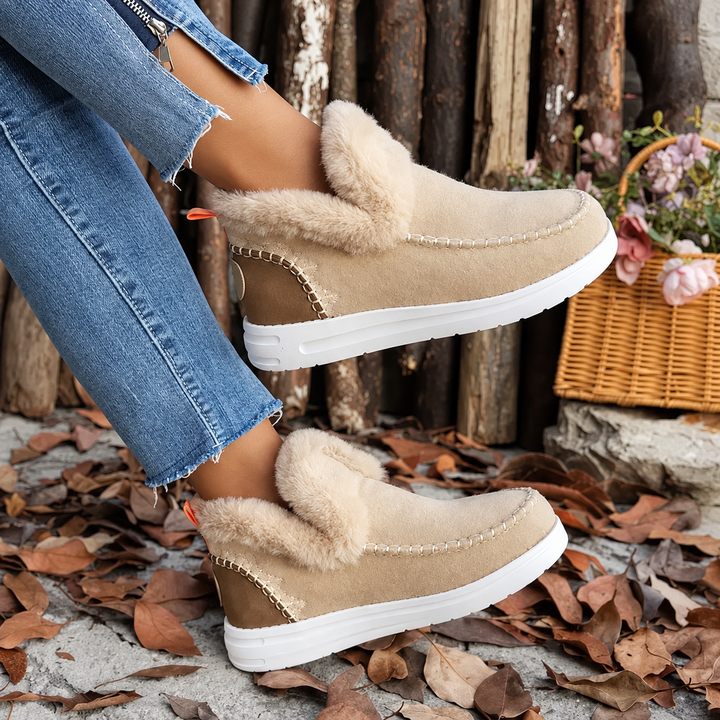 Beige ruskindslignende sneakers med blød plyskant og hvid sål, båret med jeans foran en kurv med blomster. 3
