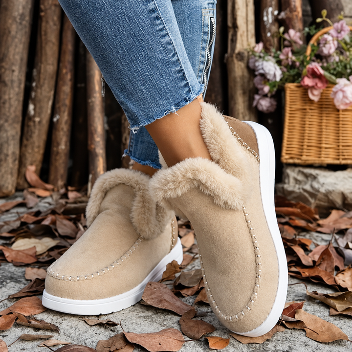 Beige sneakers med plysfor og hvid sål, båret med jeans, set skråt forfra mellem efterårsblade. 9