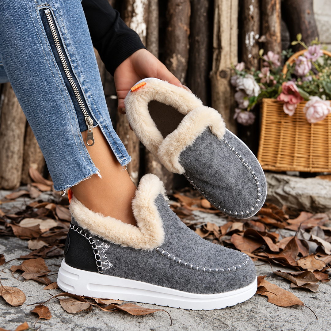 Grå slip-on sneakers med plysfor og sort hælkappe, hvor modellen holder den ene sko op og viser foret. 5