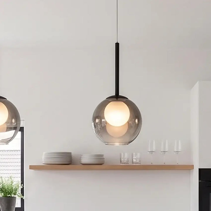 Nærbillede af en tændt røggrå glaskuglelampe over en træhylde med tallerkener og glas 11