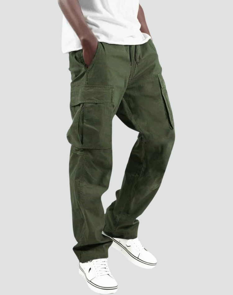 Model i olivengrønne cargobukser med store sidelommer og snøre i taljen, hvid T-shirt og hvide sneakers, set fra siden. 1