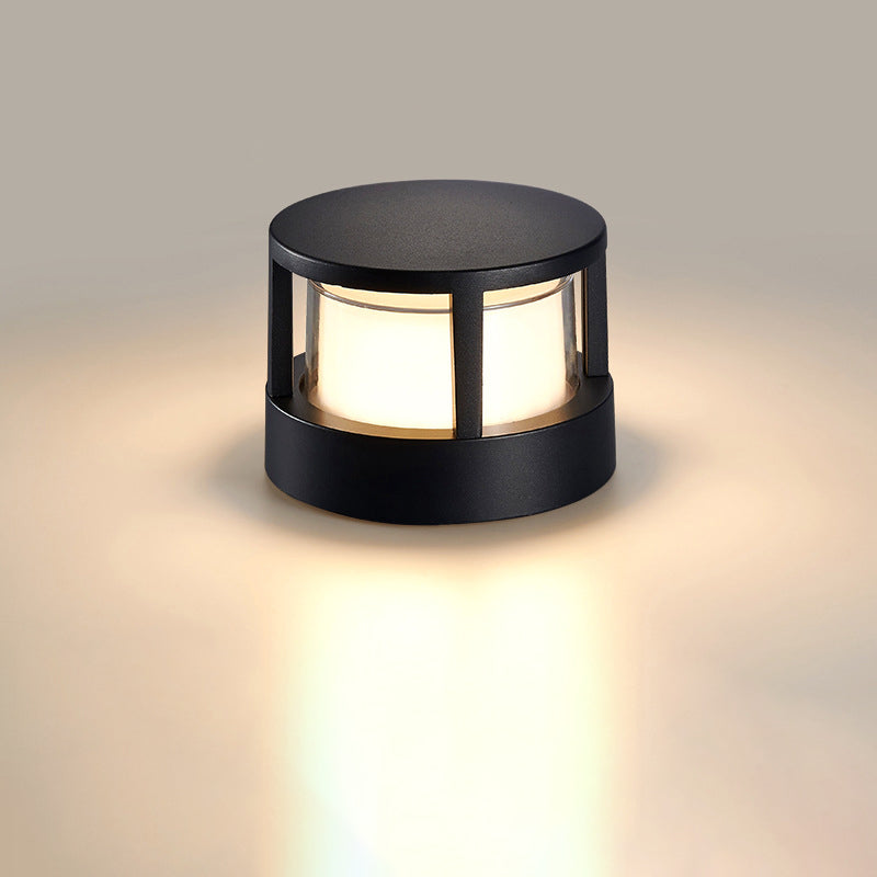 Rund sort lampe med lukket låg og gitterramme lyser varmt mod neutral baggrund. 8