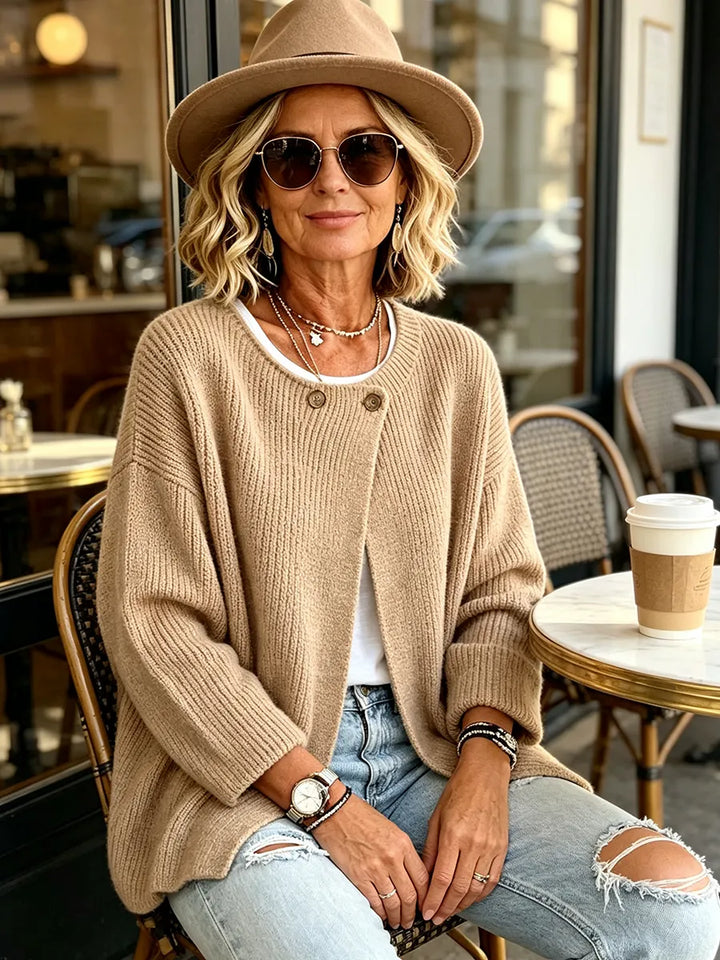 Model i kamelfarvet cardigan, hat og solbriller sidder ved et cafébord udendørs 5