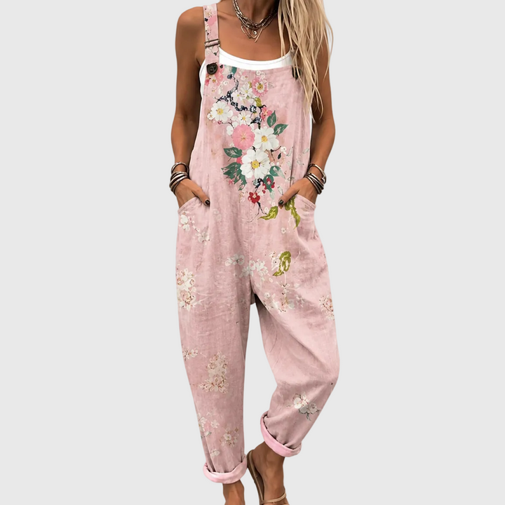 Nærbillede af modellen forfra i de lyserøde overalls med store blomster på brystet, hænderne i sidelommerne og oprullede ben. 1