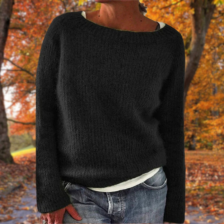 Kvinde i sort strikket sweater med rund hals, båret over hvid trøje og jeans i efterårsskov. 2