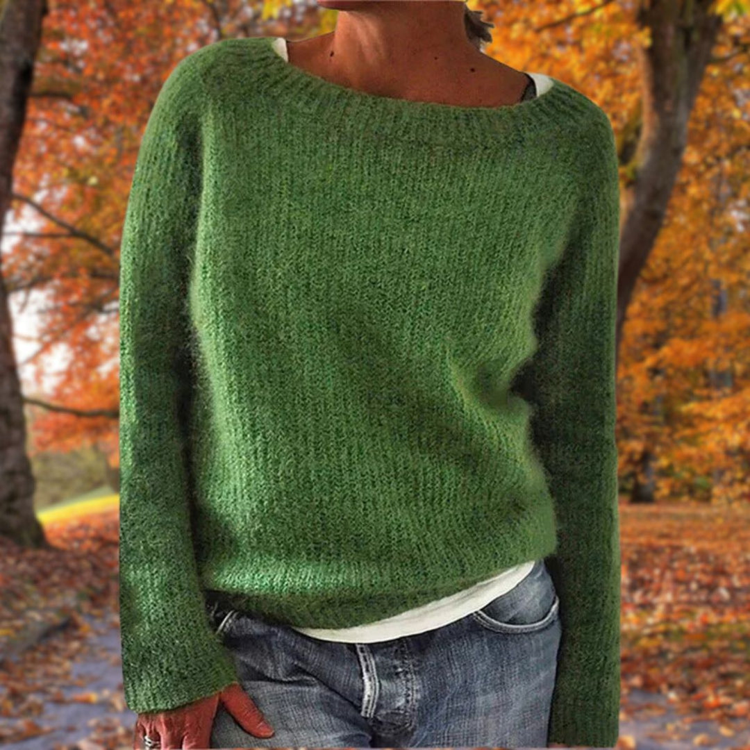 Kvinde i grøn strikket sweater med rund hals, båret over hvid trøje og jeans i efterårsskov. 5