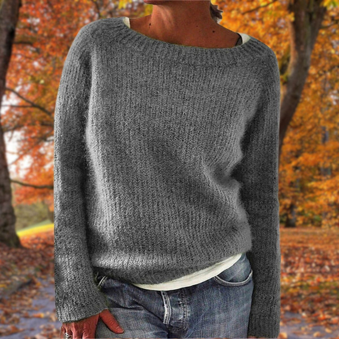 Kvinde i grå strikket sweater med rund hals, båret over hvid trøje og jeans i efterårsskov. 4