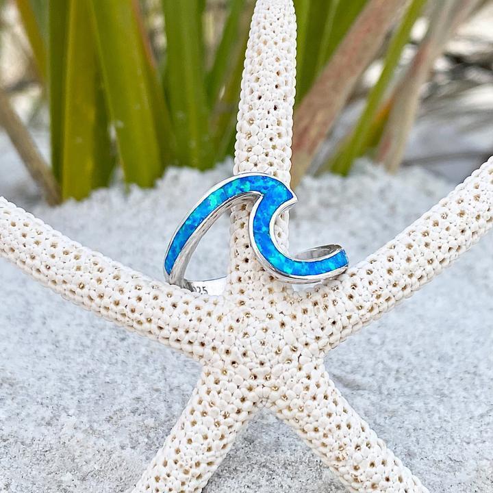 Silberner Wellenring mit blauem Opal auf Seestern im Sand, maritimer Schmuck, Strandaccessoire.