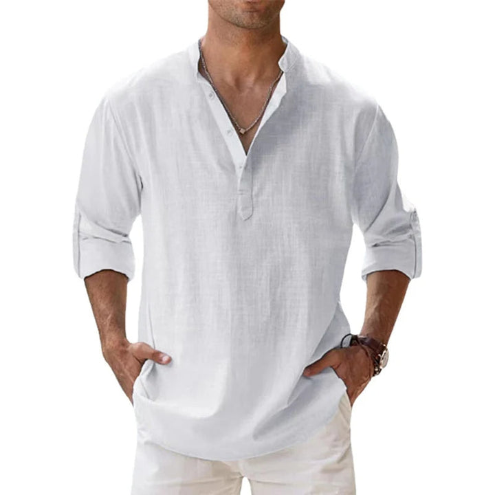 Mand i hvid langærmet hørskjorte med stå-krave og knaplukning, ærmerne smøget op og hænderne i lommerne. 4