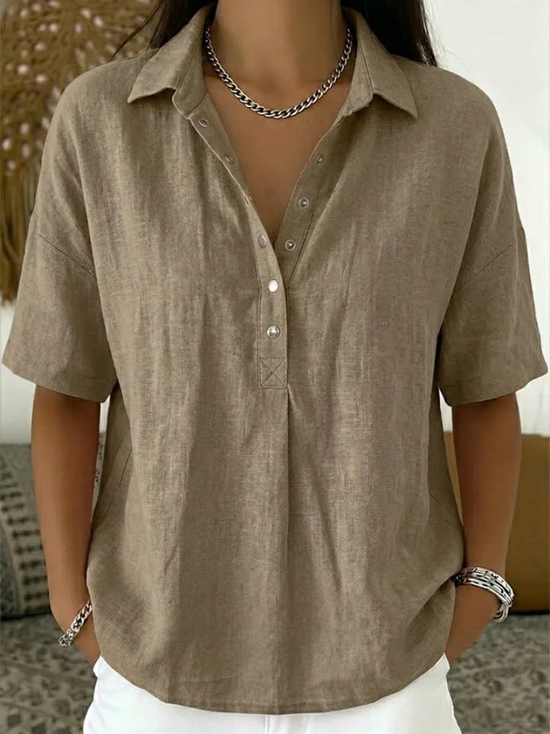 Samme bluse i sandbeige med krave og metalknapper, båret af model med hænderne i lommerne 2