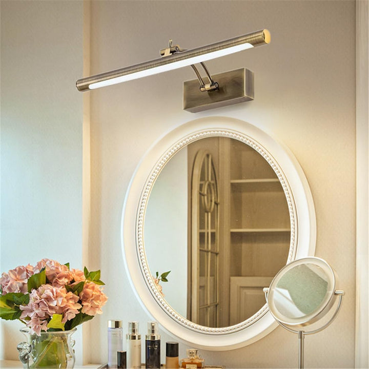 Rørformet lampe i antik finish over et ovalt spejl på en kommode med blomster 6