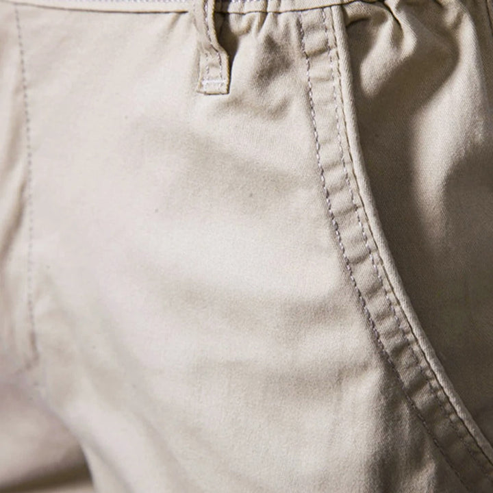 Nærbillede af sidelommen og bælteløkken på beige shorts med tydelige kontrastsyninger. 3