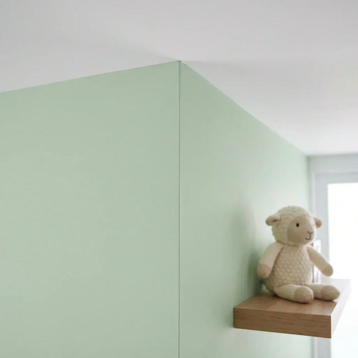 Skarp lige malingskant i hjørnet mellem en lysegrøn væg og et hvidt loft, med en tøjfår på en hylde 5