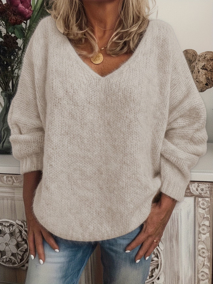 Kvinde i lys beige blød strikbluse med dyb V-hals og løs pasform, båret til blå jeans. 4