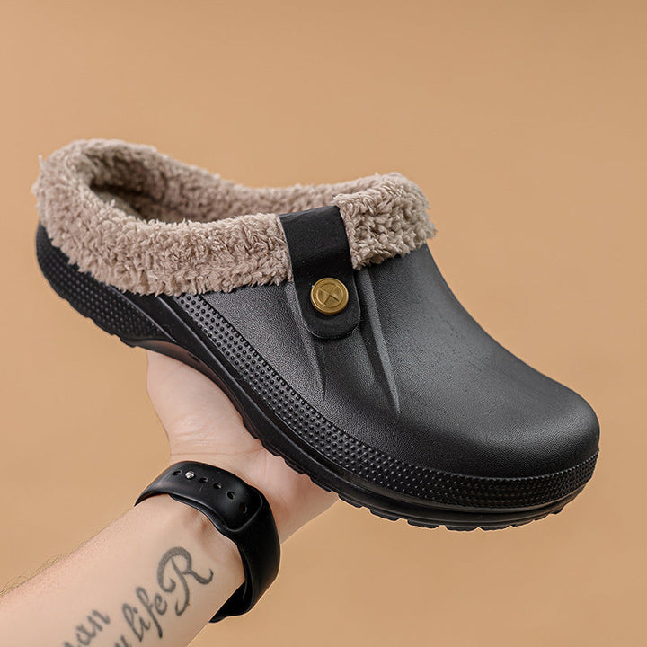 Sort klipklapper med lys fleecekant holdt i en hånd mod beige baggrund, set fra siden. 2