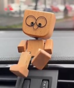 Nærbillede af træfigur med store øjne, der sidder på bilens instrumentbrædt med det ene ben hængende ned over kanten. 6