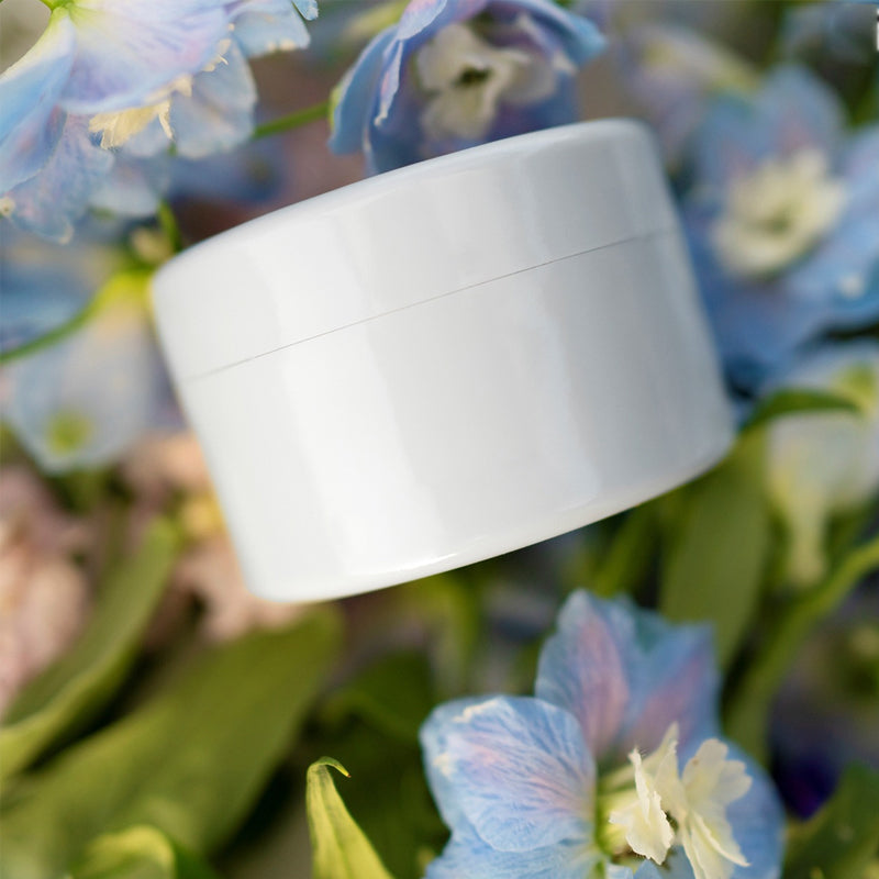 Hvid rund indsats ligger ovenpå blå og hvide rittersporeblomster og grønne blade. 9