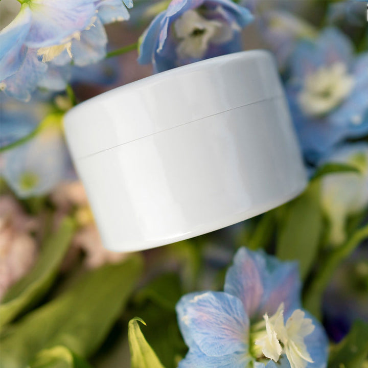 Hvid rund indsats ligger ovenpå blå og hvide rittersporeblomster og grønne blade. 15
