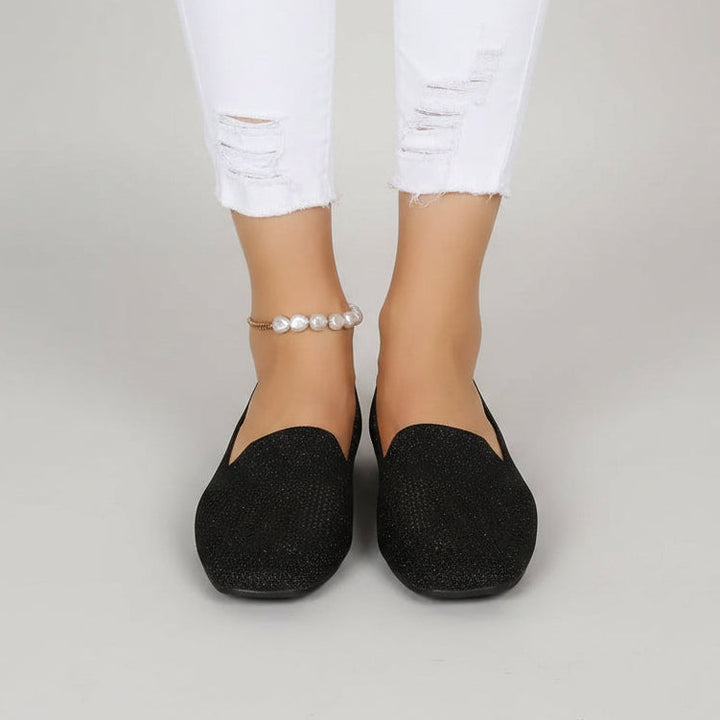 Sorte slip-on sko med firkantet tå set forfra på en model i hvide flossede jeans og perleanklet. 2