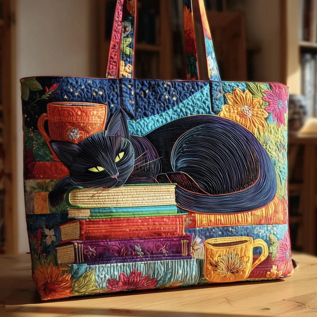 Farverig vatteret totebag set forfra på et træbord, med en sovende sort kat på en bunke bøger mellem to krus og blomster. 1