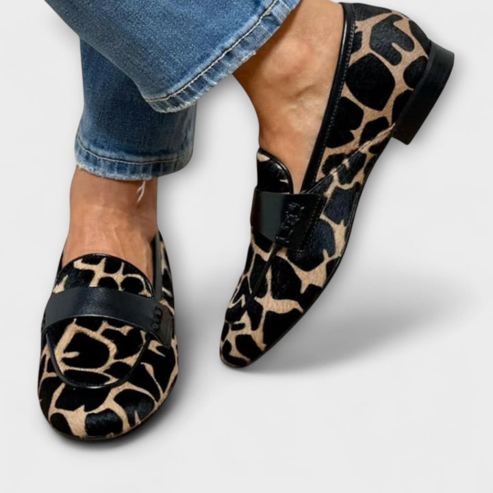 Begge loafere set fra oven og foran med sort kant, flad hæl og dyremønstret overdel, båret til jeans. 3