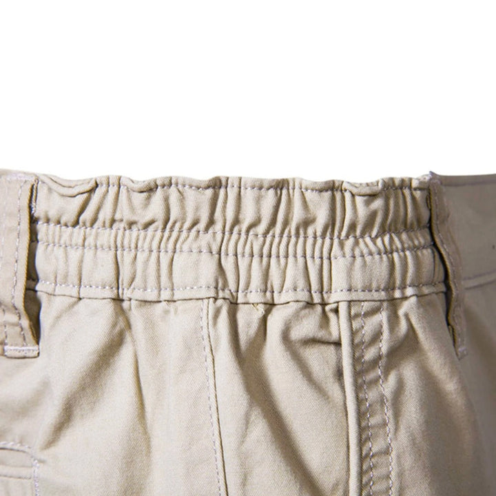 Nærbillede af den elastiske, rynkede linning på beige shorts med bælteløkker og syninger. 4