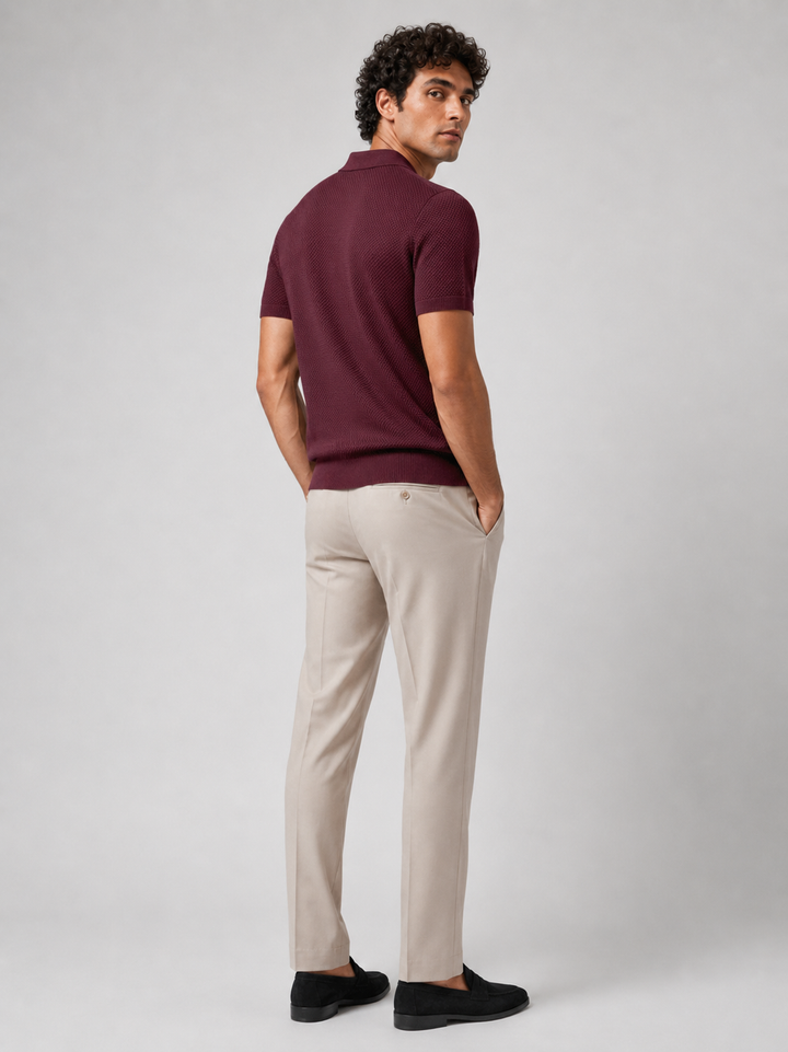 Model i bordeaux strikpolo set bagfra, kigger over skulderen, med beige bukser og sorte loafers 24