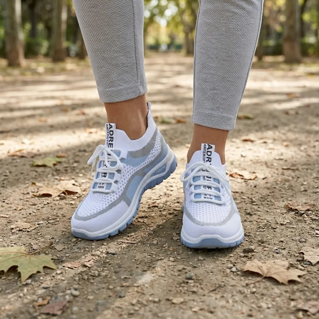 Hvide sneakers med blå sål båret af en kvinde i grå leggings på en sti med efterårsblade. 2