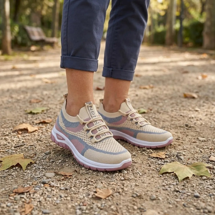 Kvinde i oprullede blå bukser går på en grusset sti med efterårsblade i beige sneakers med lyserød sål. 29
