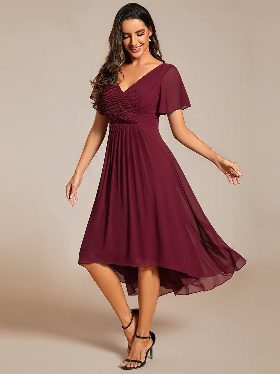 Model i bordeaux chiffonkjole med V-hals ser smilende nedad, mens nederdelen svinger og den asymmetriske kant fremhæves. 47