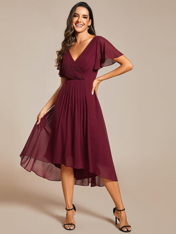 Model i bordeaux kjole med hånd på hoften og løftet nederdel, så den gennemsigtige chiffon i den høj-lave kant ses. 48