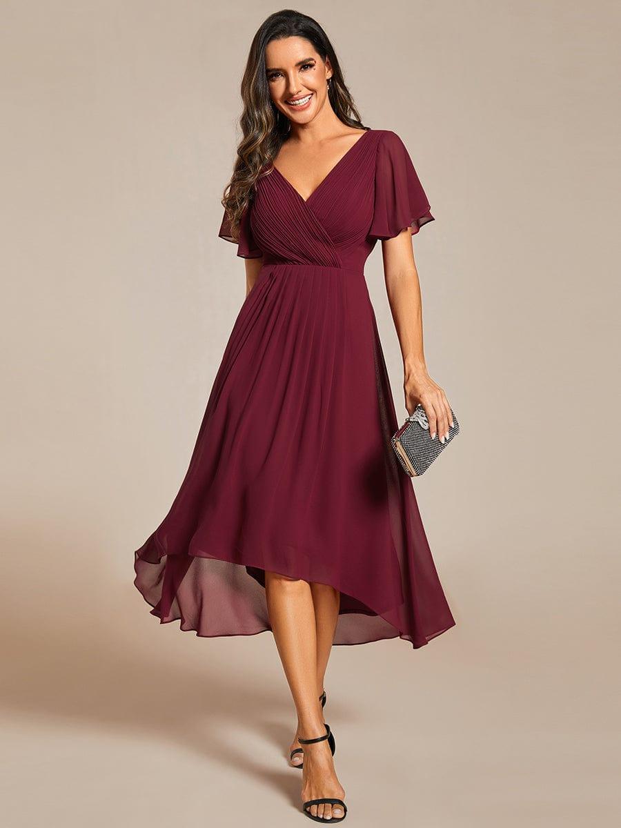 Bordeauxrød chiffonkjole med plisseret overdel og korte flagrende ærmer set forfra, model holder en glitrende clutch. 3