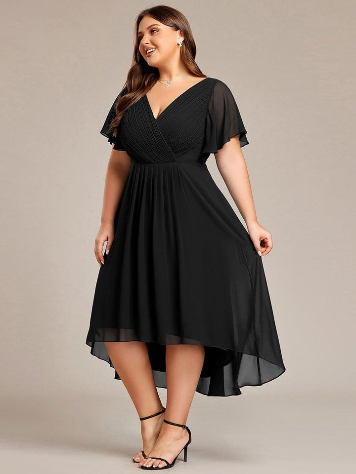 Sort kjole i plussize set fra siden på smilende model, der holder let i nederdelen. 29