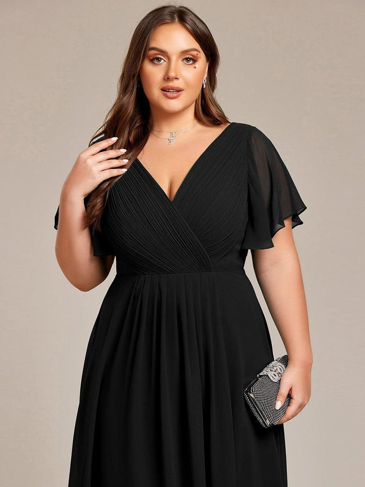 Nærbillede af sort kjoles plisserede V-hals og flagrende ærmer på plussize-model med funklende clutch. 28