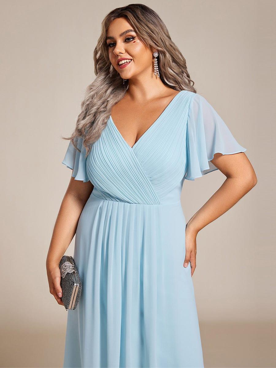 Nærbillede af lyseblå kjoles plisserede overdel og vingeærmer på smilende plus size-model med clutch. 91