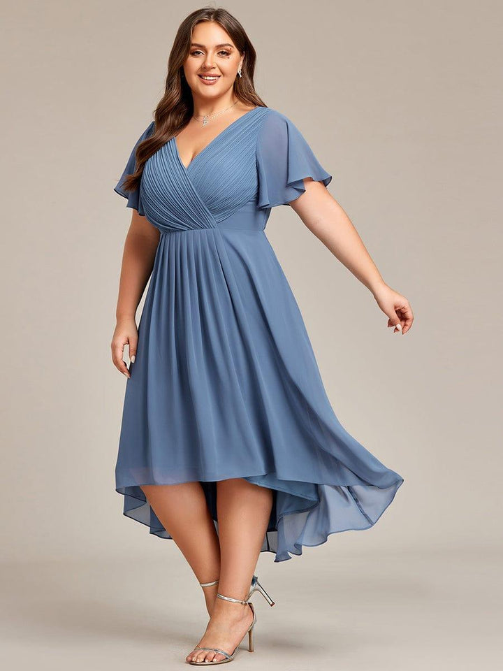 Model i stor størrelse i dueblå kjole set fra siden, mens den lette chiffonnederdel svinger og den asymmetriske kant ses. 45