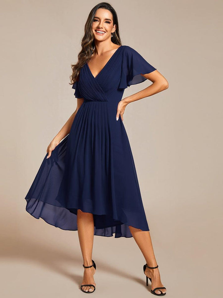 Model i marineblå kjole med hånd på hoften og løftet nederdel, så den lette chiffon i den høj-lave kant ses. 54
