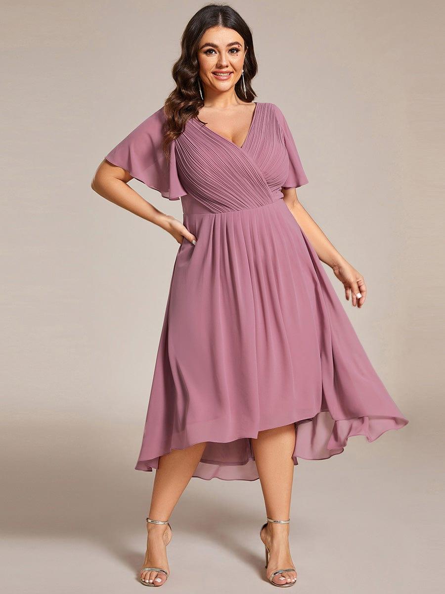Plus size-model i mauve kjole med hånden på hoften, set forfra med fald der er kortere foran og længere bagpå. 66