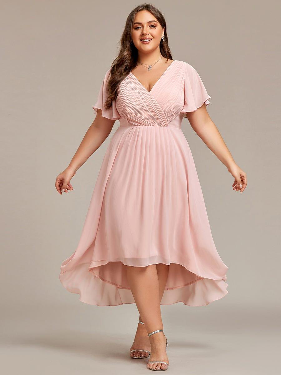 Lyserød kjole i plussize på model med udstrakte arme, så den flagrende asymmetriske nederdel ses. 35