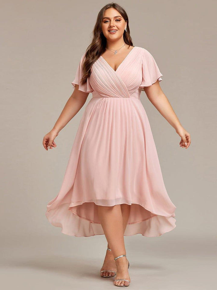 Lyserød kjole i plussize på model med udstrakte arme, så den flagrende asymmetriske nederdel ses. 35