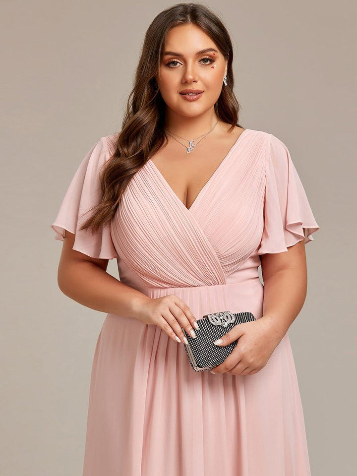 Nærbillede af lyserød kjoles plisserede overdel og V-hals på plussize-model, der holder en glitrende clutch. 33
