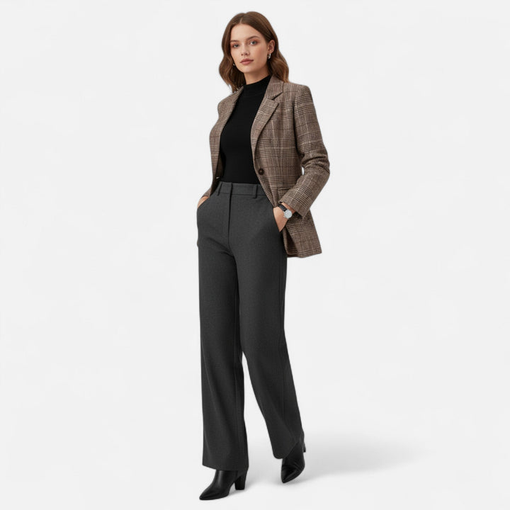 Model i fuld figur set forfra i ternet blazer, sort top, grå vidde bukser og sorte støvler med hænderne i lommerne. 2