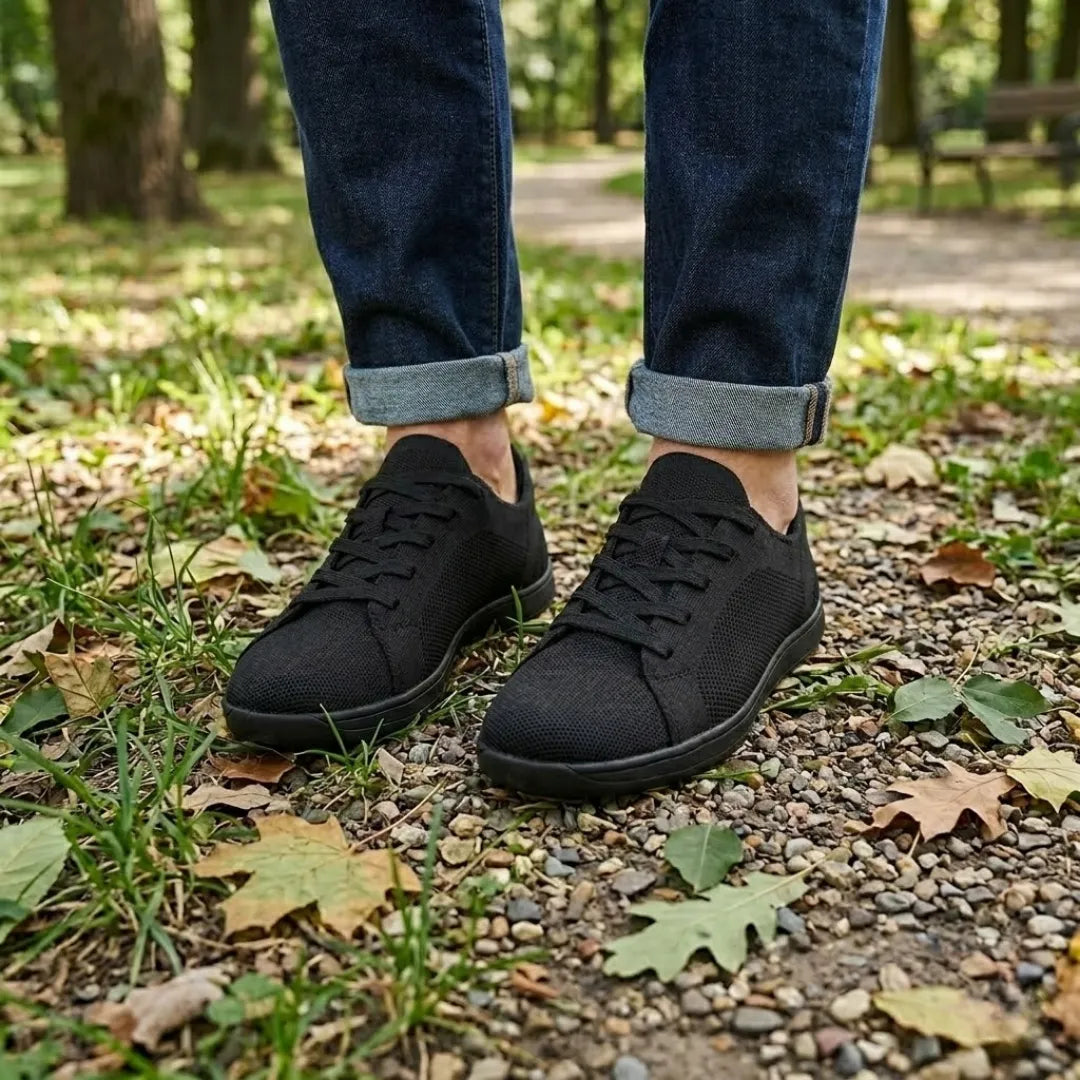 Sorte strikmesh-sneakers båret af en person i oprullede mørkeblå jeans på en grussti med visne blade. 11