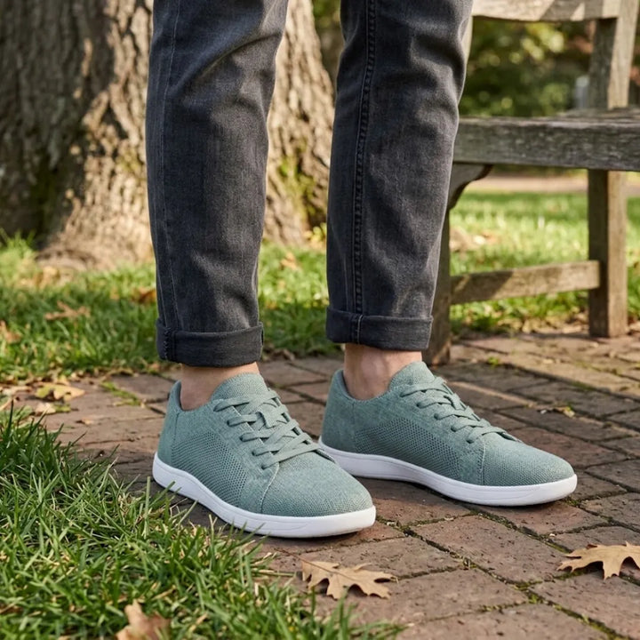 Model i mørke jeans går i grønne mesh-sneakers med hvid sål på en teglbelagt sti i en park. 29