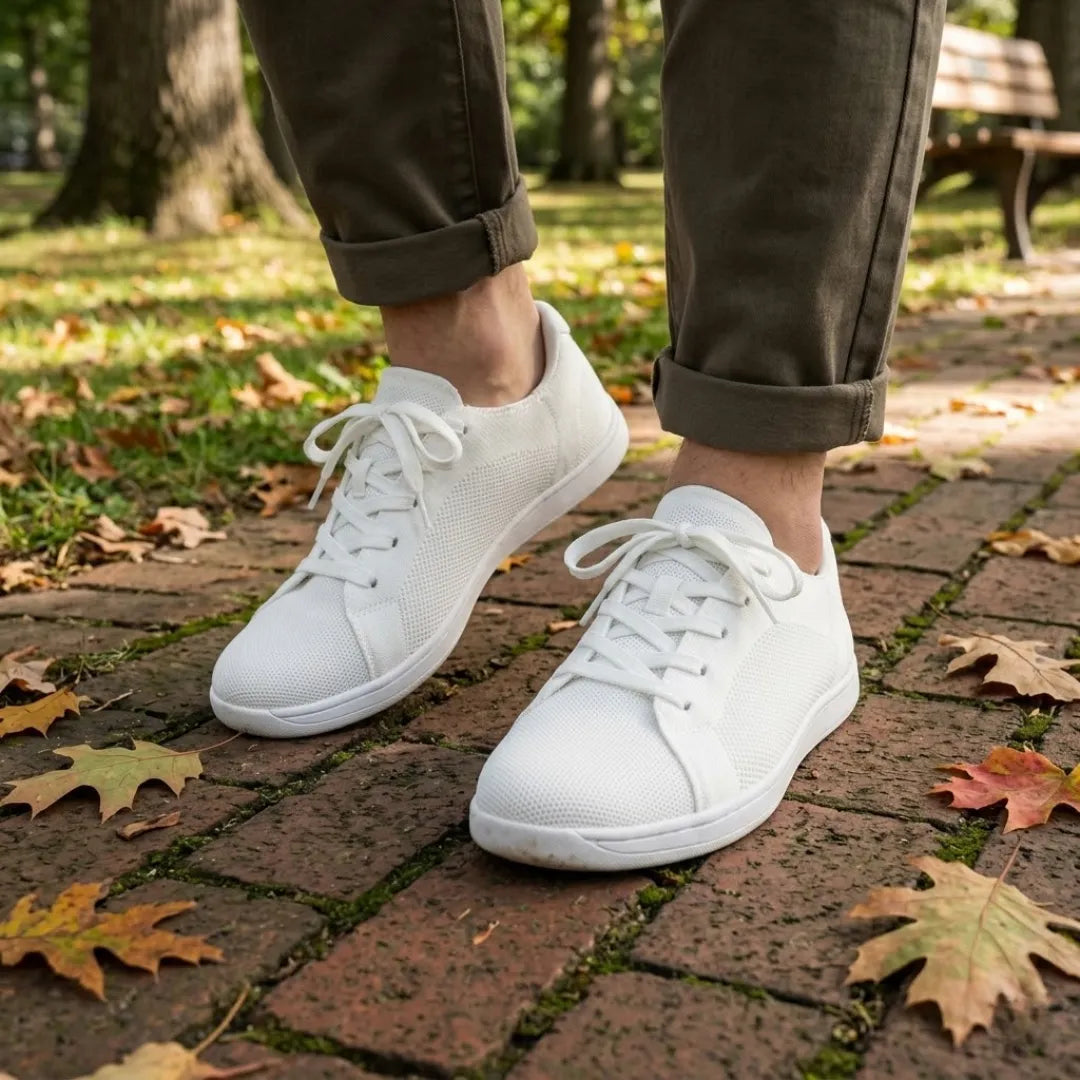 Model i olivengrønne bukser går i hvide mesh-sneakers på en teglbelagt sti med efterårsblade. 38