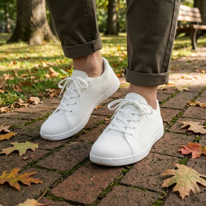 Model i olivengrønne bukser går i hvide mesh-sneakers på en teglbelagt sti med efterårsblade. 38